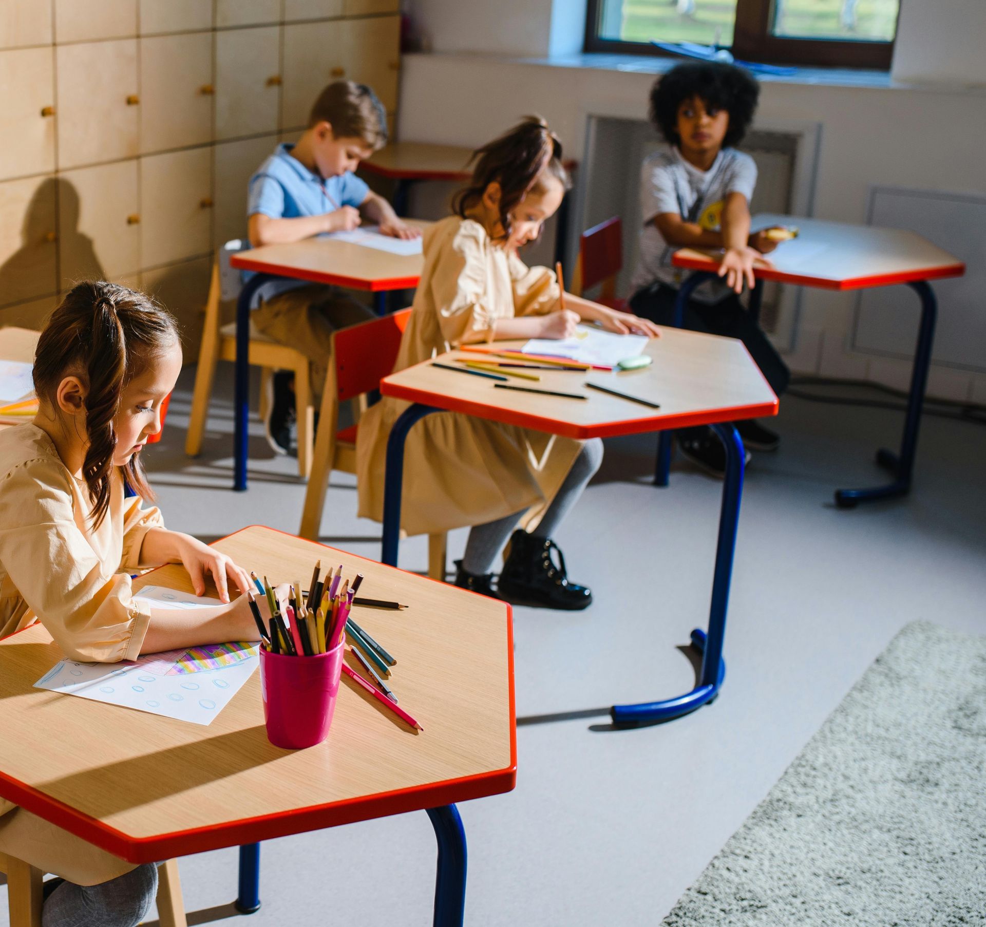 A group of diverse children sitting in a classroom, actively learning and drawing at their desks.