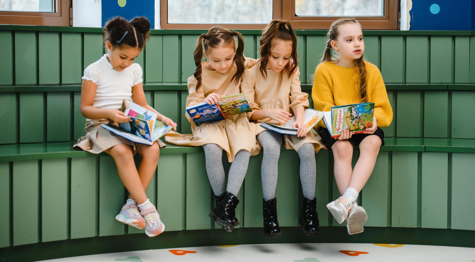 Group of young girls sitting indoors, reading and studying in a classroom setting.