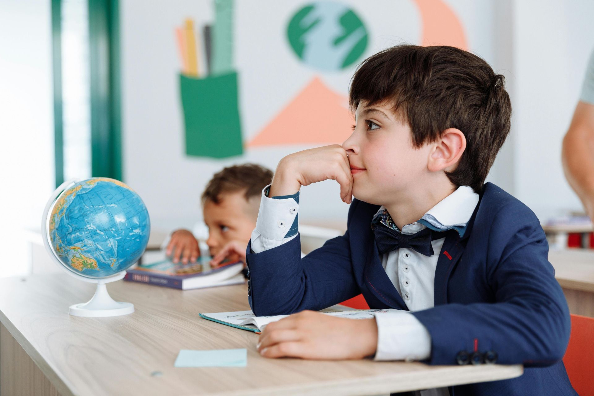 Two boys engaged in a classroom setting with books and a globe, learning about geography.