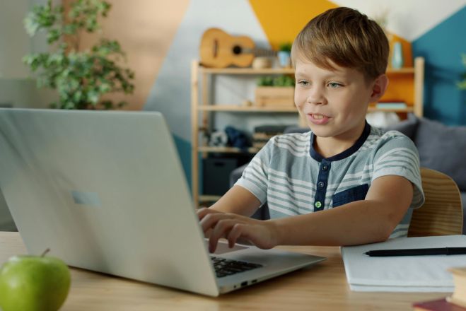 Young boy using a laptop for online learning at home with study materials nearby.